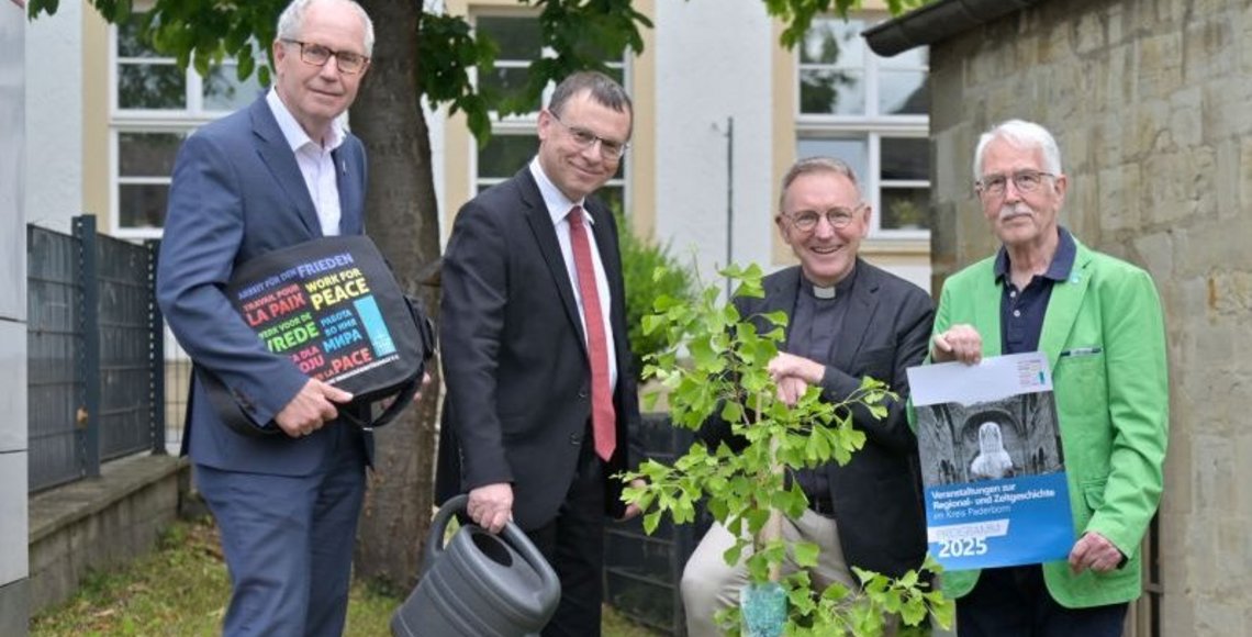 Das Foto zeigt einen jungen Ginkgo-Baum am Forum St. Liborius, der von (v.l.n.r.) Landrat a. D. Manfred Müller, Pfarrer Dr. Eckhard Düker (Evangelischer Kirchenkreis Paderborn), Dechant und Domkapitular Benedikt Fischer (Erzbistum) und Hermann-Josef Bentler als Kreisvorstandsmitglied des Volksbundes) gepflanzt wurde. Pfarrer Dr. Eckhard Düker gießt den Baum noch, während Dechant und Domkapitular Benedikt Fischer den Spaten der Baumpflanzaktion noch in den Händen hält.